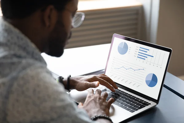 A man with glasses sits at a laptop and analyzes the chart